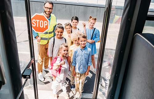 Kinder stehen mit Schülerlotsen vor dem Eingang eines Busses.