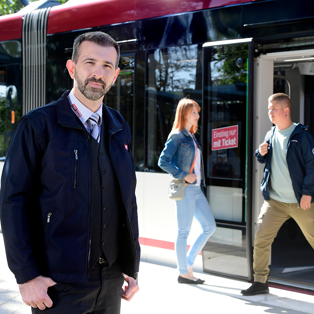 Fahrer vor Straßenbahn. Im Hintergrund Aus- und Einstieg von Fahrgästen.