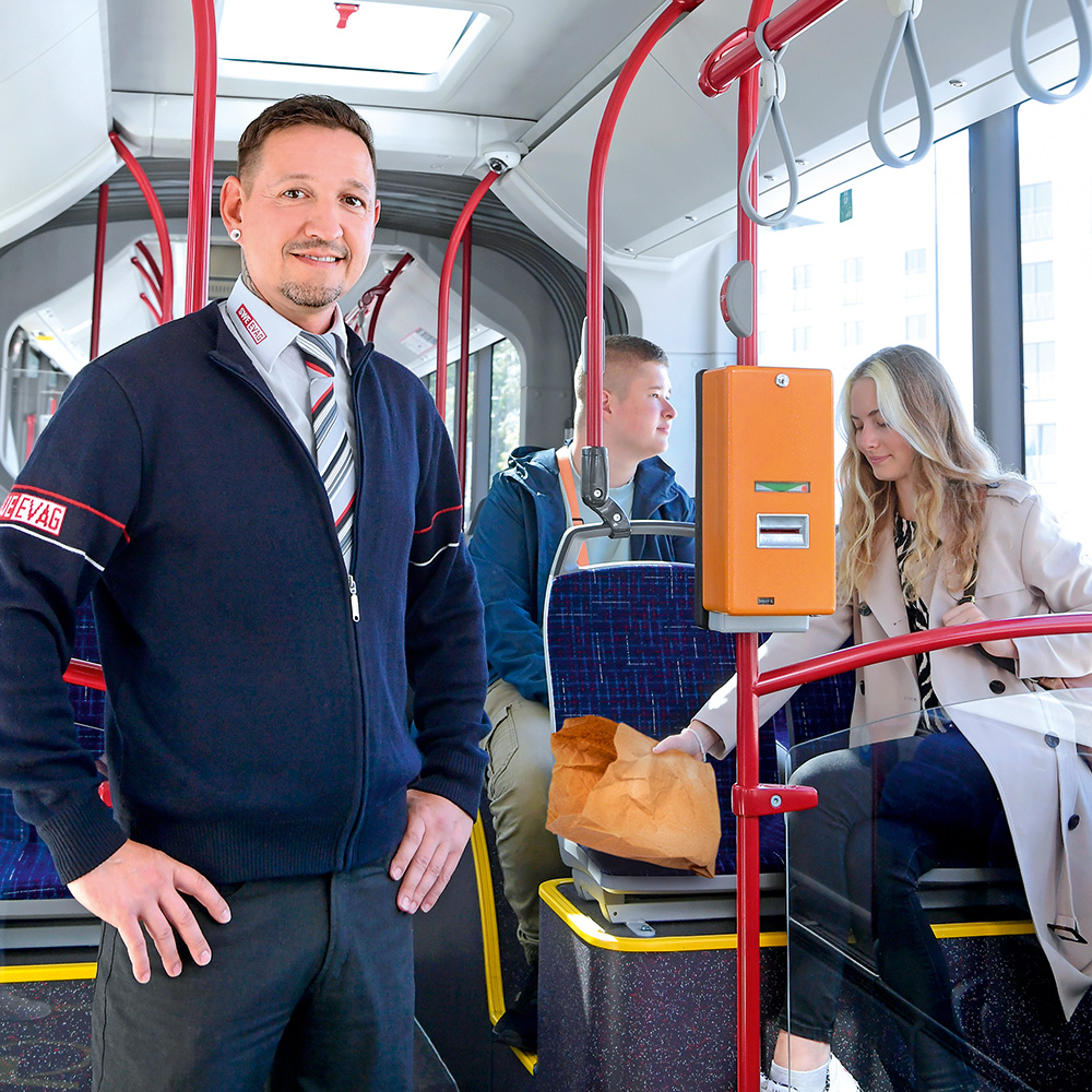 Fahrer im Bus. Im Hintergrund Fahrgast, der seinen Müll wieder mitnimmt.