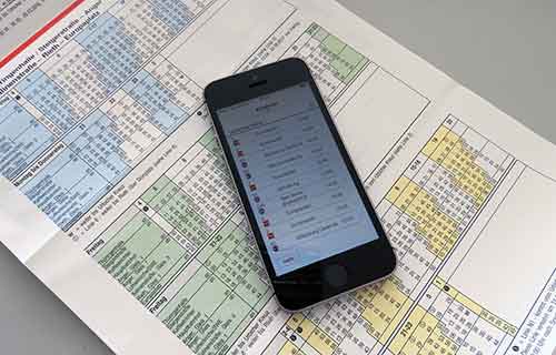Aufgeklappter Fahrplanflyer. Darauf liegt ein Handy, dass einen Fahrplan zeigt.